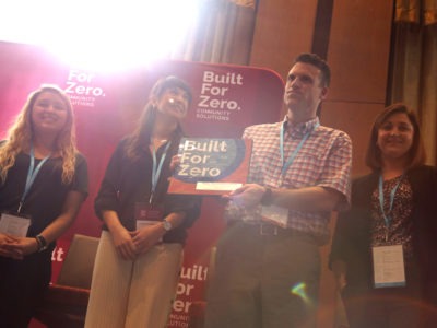 Team member holding up Built for Zero signage on stage at a conference
