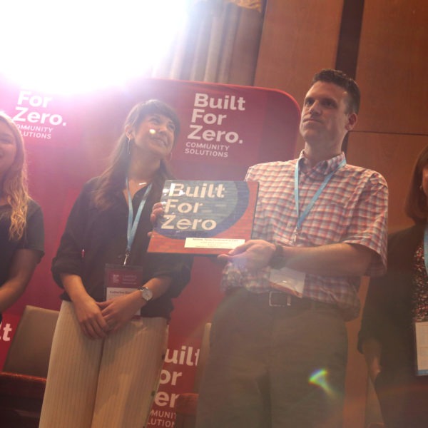 Team member holding up Built for Zero signage on stage at a conference
