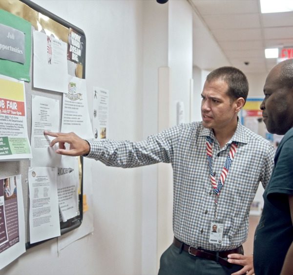 Two men looking at bulletin board with papers